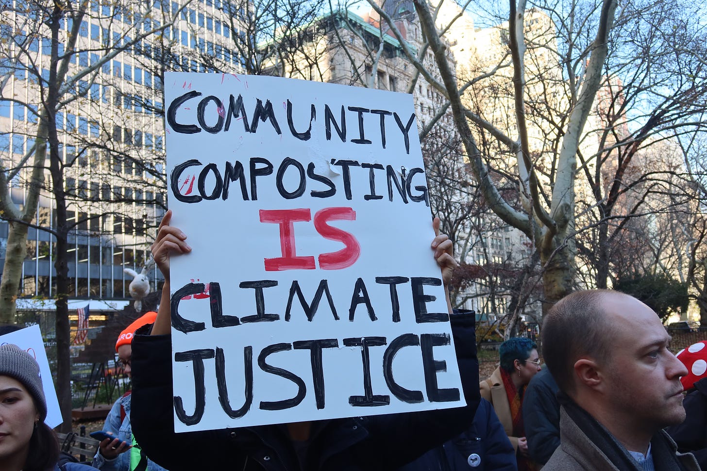 A protestor holds up a sign that reads, "Community composting is climate justice."