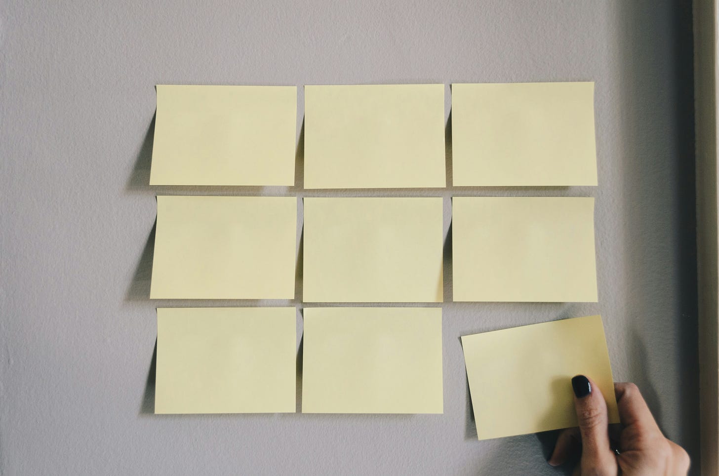 Several post-it papers on a wall and a hand with black nails that picks one