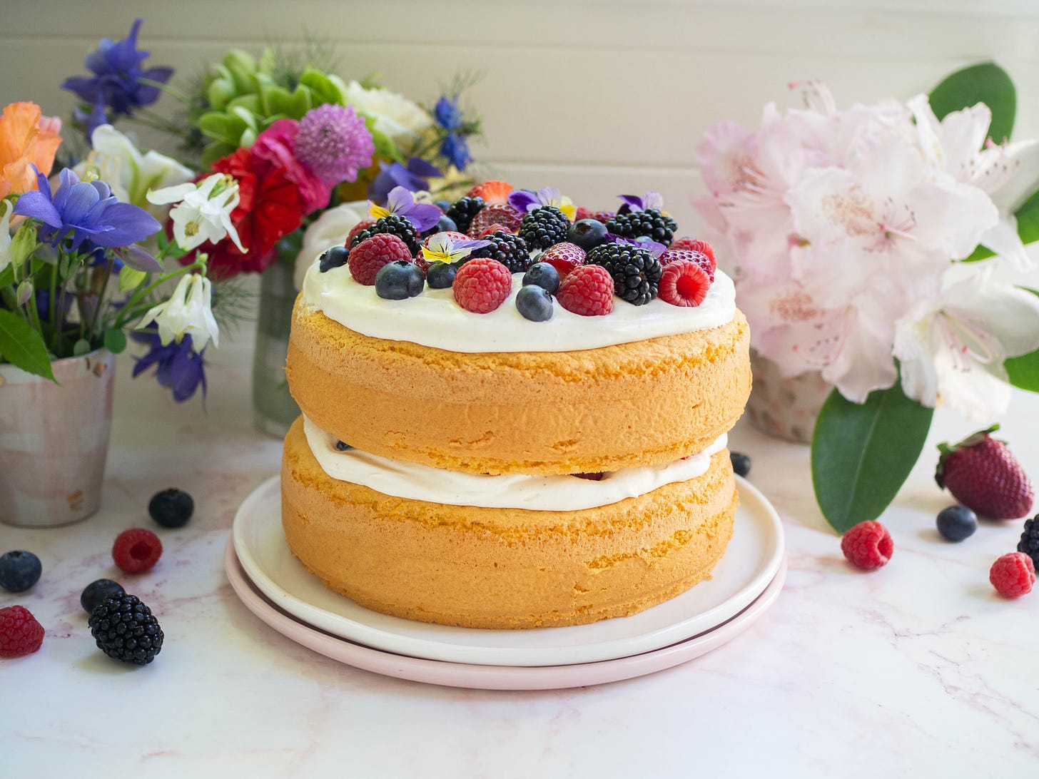 double layer sponge cake topped with berries and cream flowers in background