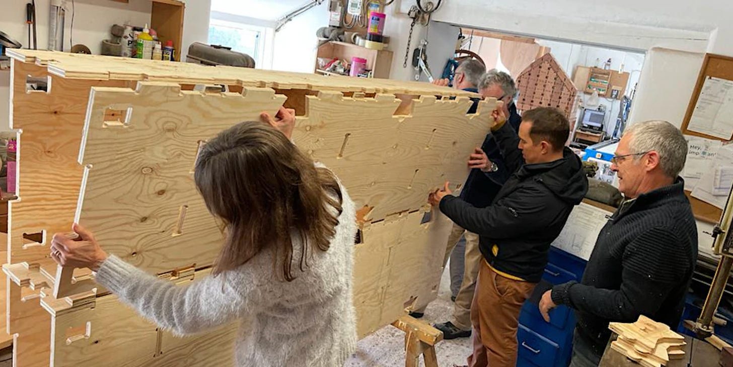 4 people hold a WikiHouse Skylark block on its side while assembling it.
