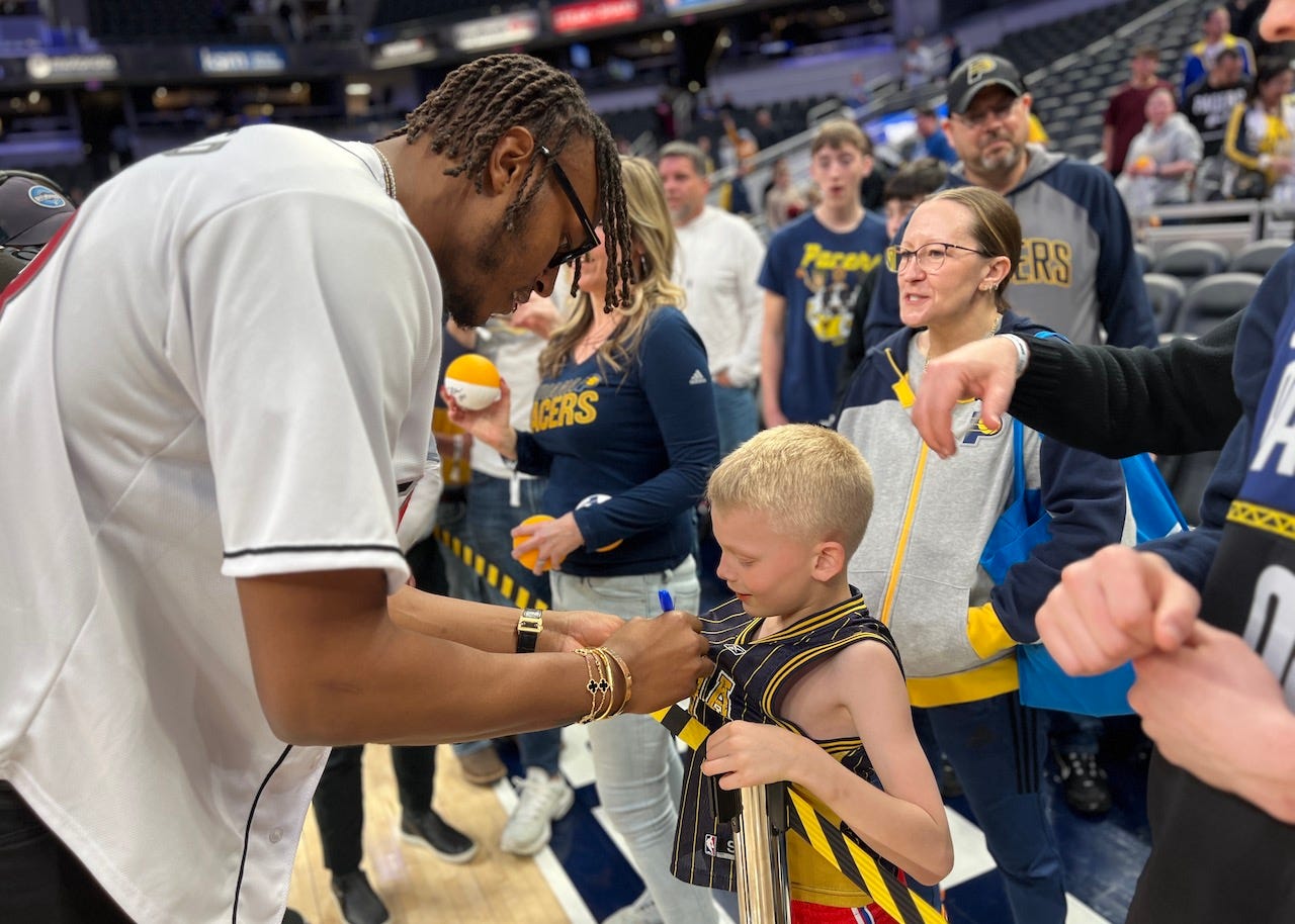 Myles Turner signs a Jermaine O’Neal jersey worn by a young Pacers fan on the court after the game.