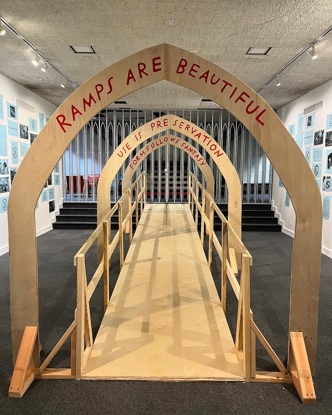 A plywood ramp with three arches. Each arch has a phrase in my handwriting. In the foreground “Ramps are beautiful,” then “Use is preservation,” and then “Form follows fantasy.” The shape of the arches is gothic (comes to a soft point at the peak), which references a shape and motif used repeatedly in the building. My understanding is that Portman was thinking about cathedrals and conceptualized the building as a modern “cathedral to art.” In this photo a narrower version of the shape is repeated in a metal grate that opens and closes at the top of the ramp.