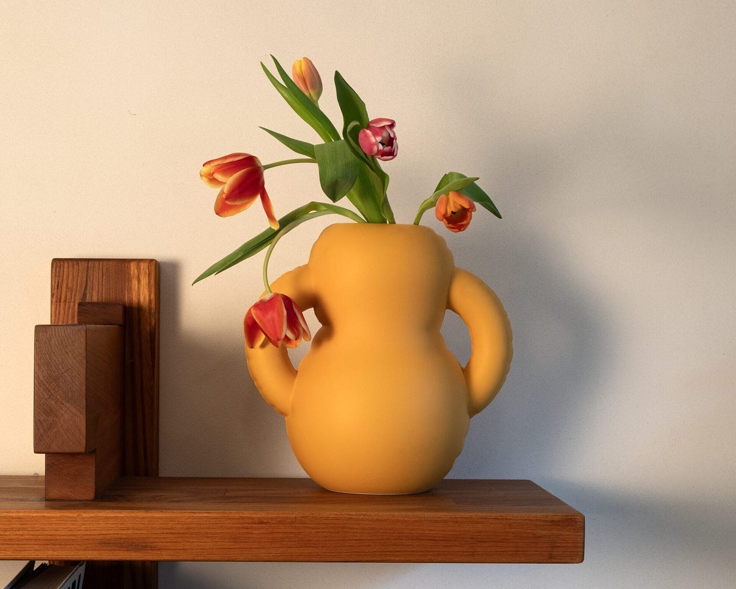 a yellow ceramic vase that looks as though it is made of inflated plastic on a shelf with tulips