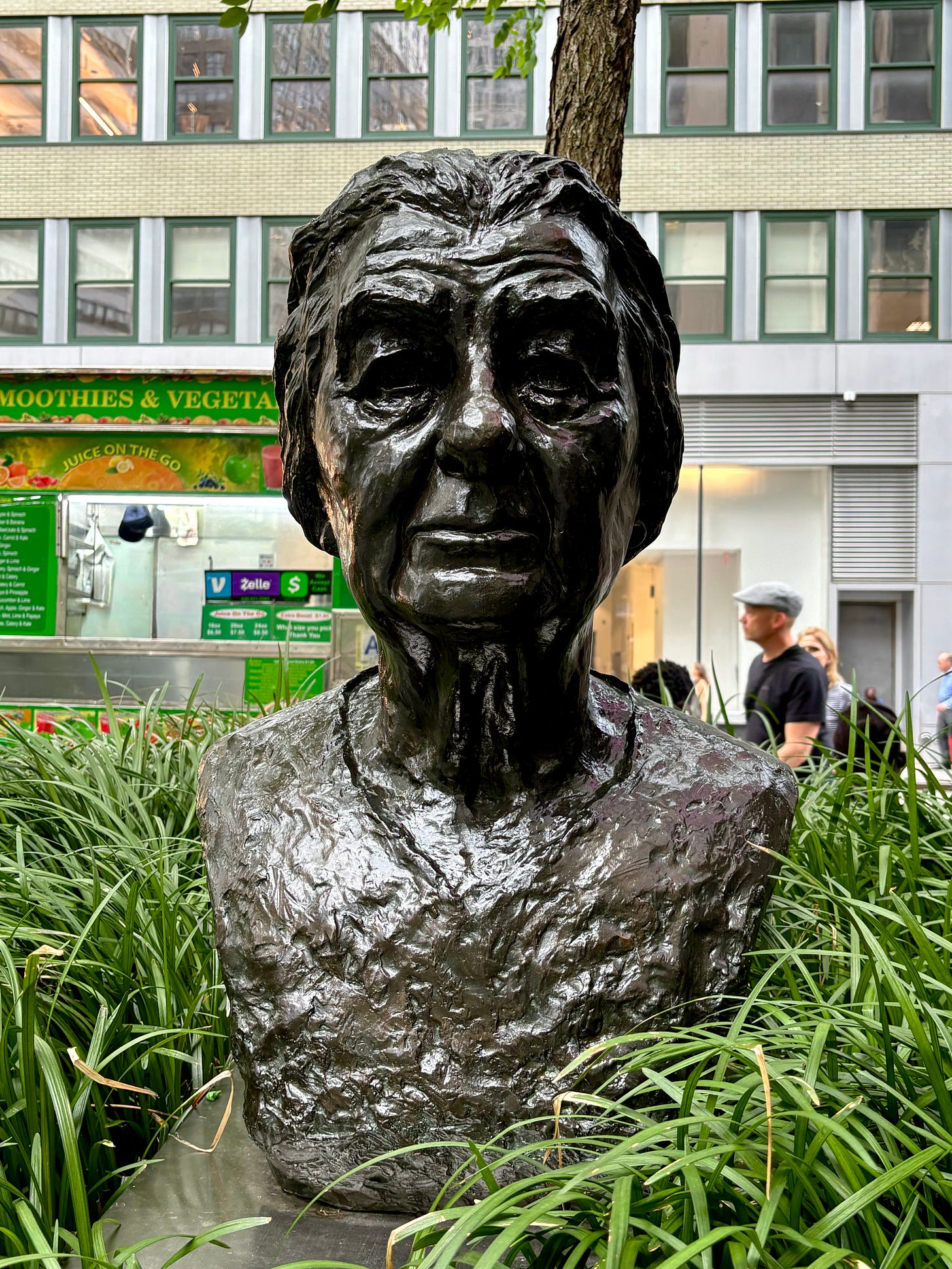 A metal bust of Golda Meir looking sever but thoughtful, resting in a planter of grass.