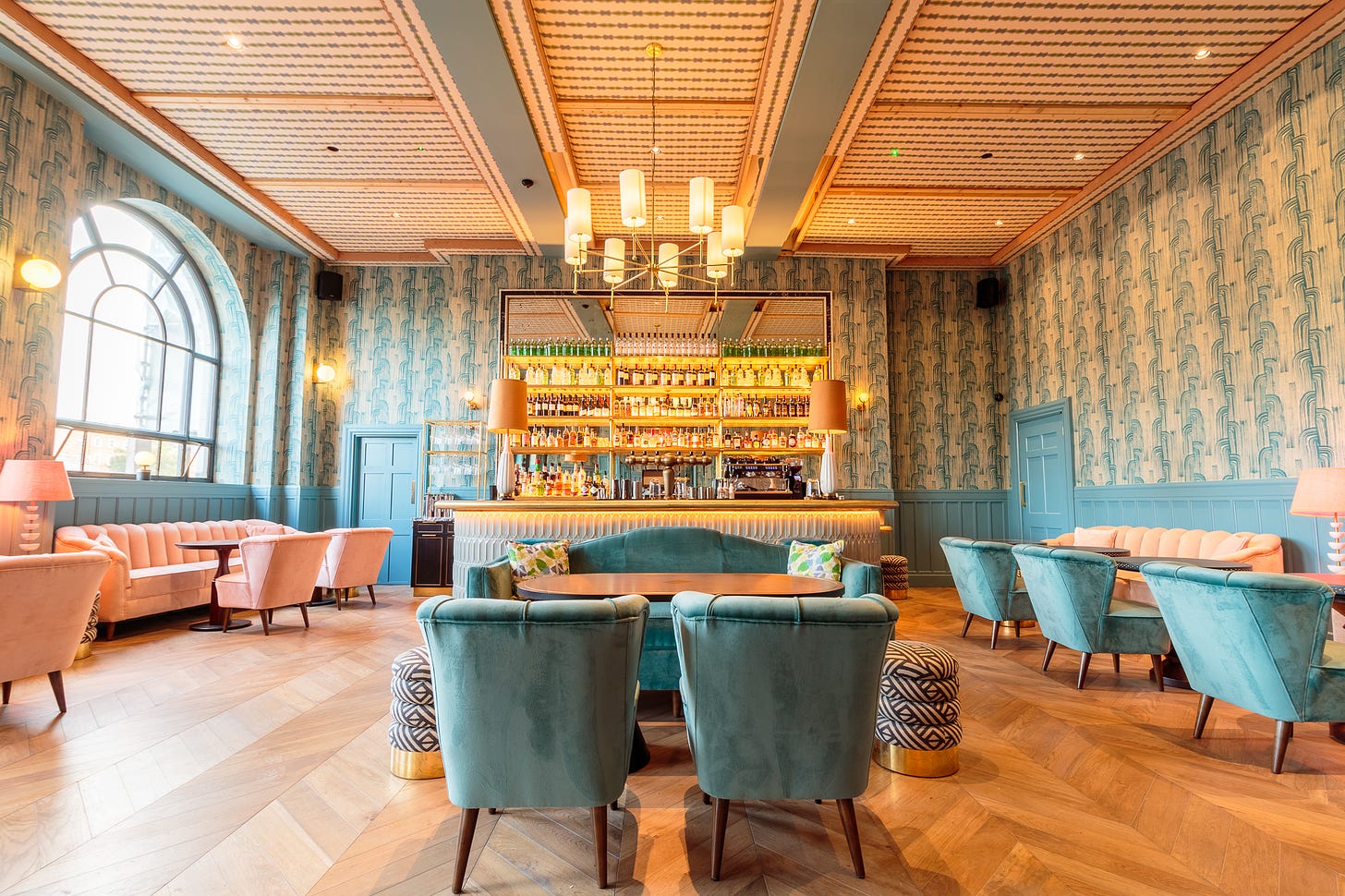 Spacious bar in hues of blue and pink, with decadent light fixtures and cosy couches and low tables