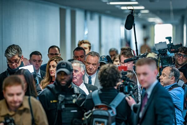 Robert F. Kennedy Jr. walking down a hall amid a crowd of people, some of whom are recording him.