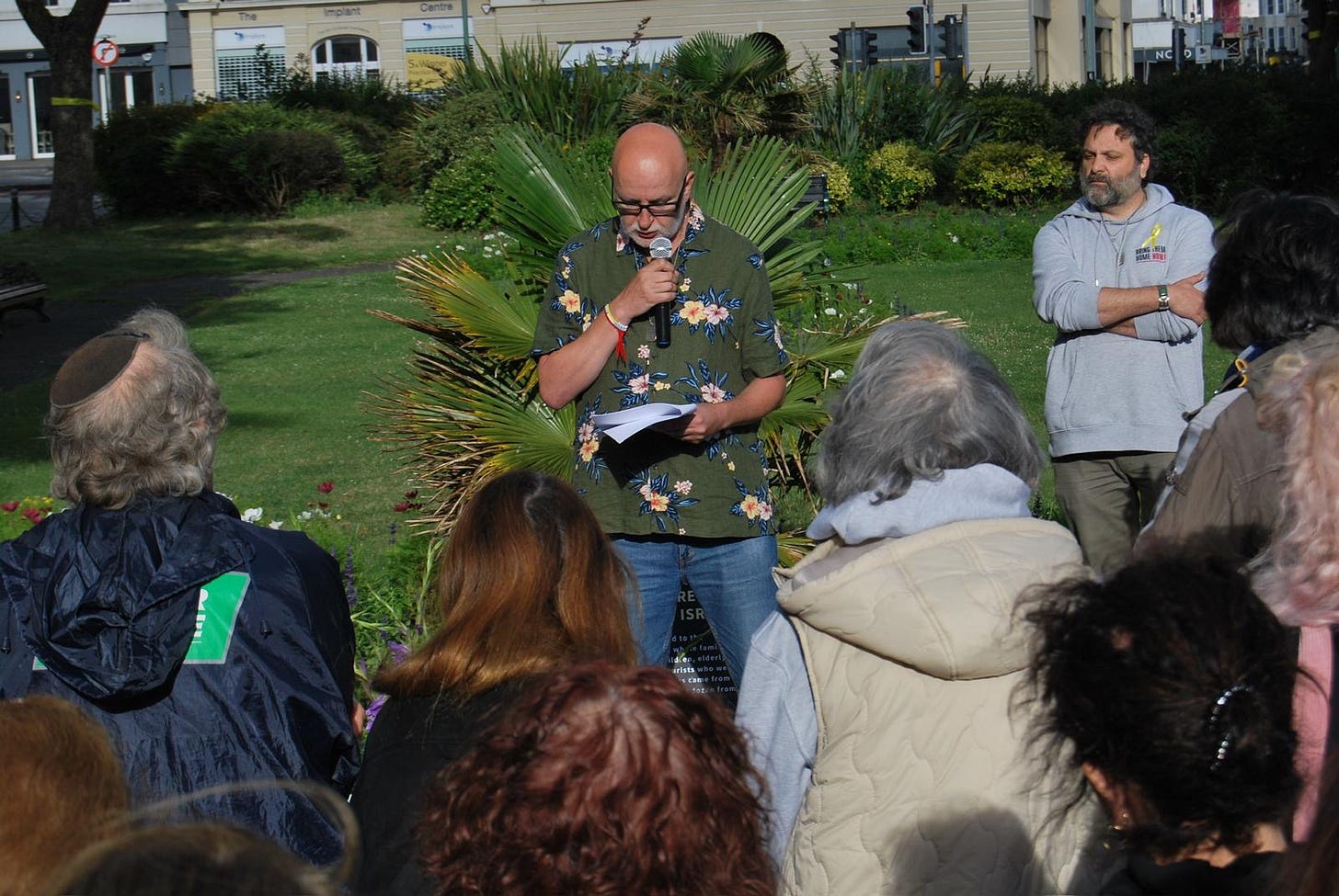 A man in his 60s with glasses and wearing a colourful shirt speaks into a microphone 