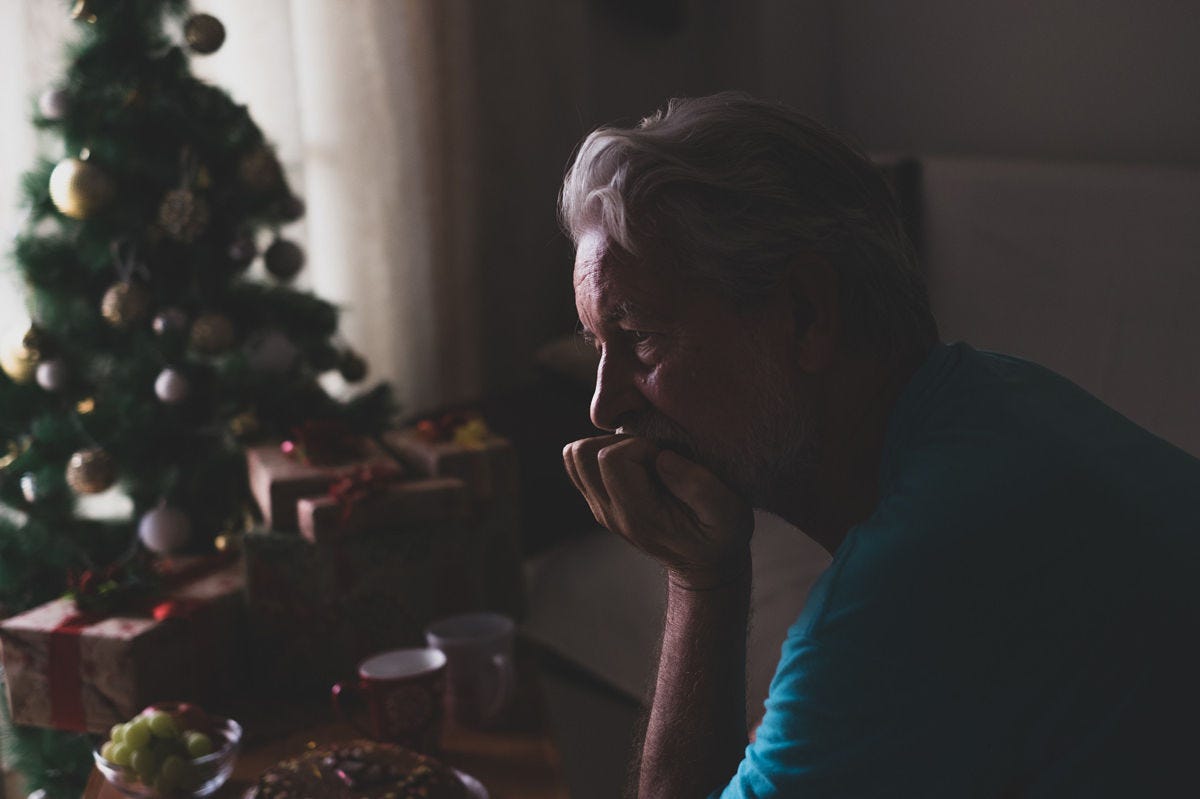 Depressed elder sitting alone near the Christmas tree.