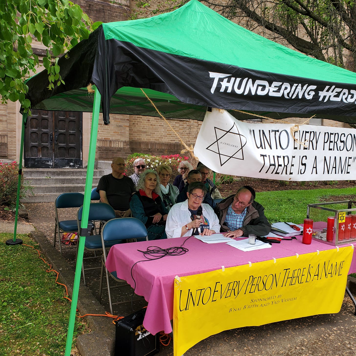 A group of nine people sit under an awning branded "Thundering Herd." There is a banner that reads "Unto every person there is a name." 