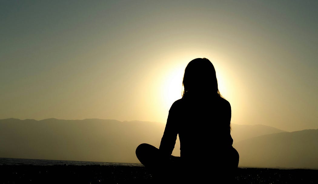 Person meditating as the Sun rises.