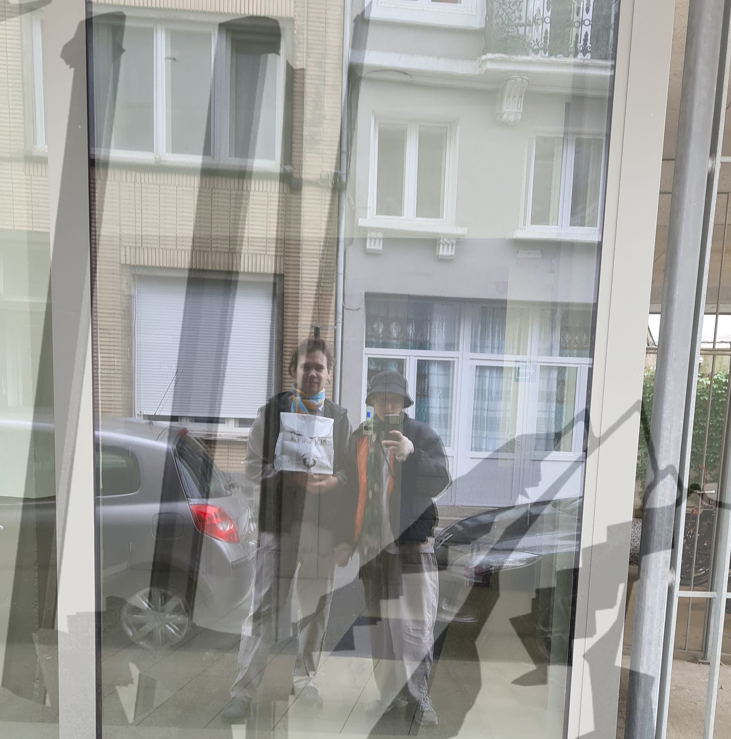 picture of a street window reflection of two people holding a white paper bag, standing between two cars