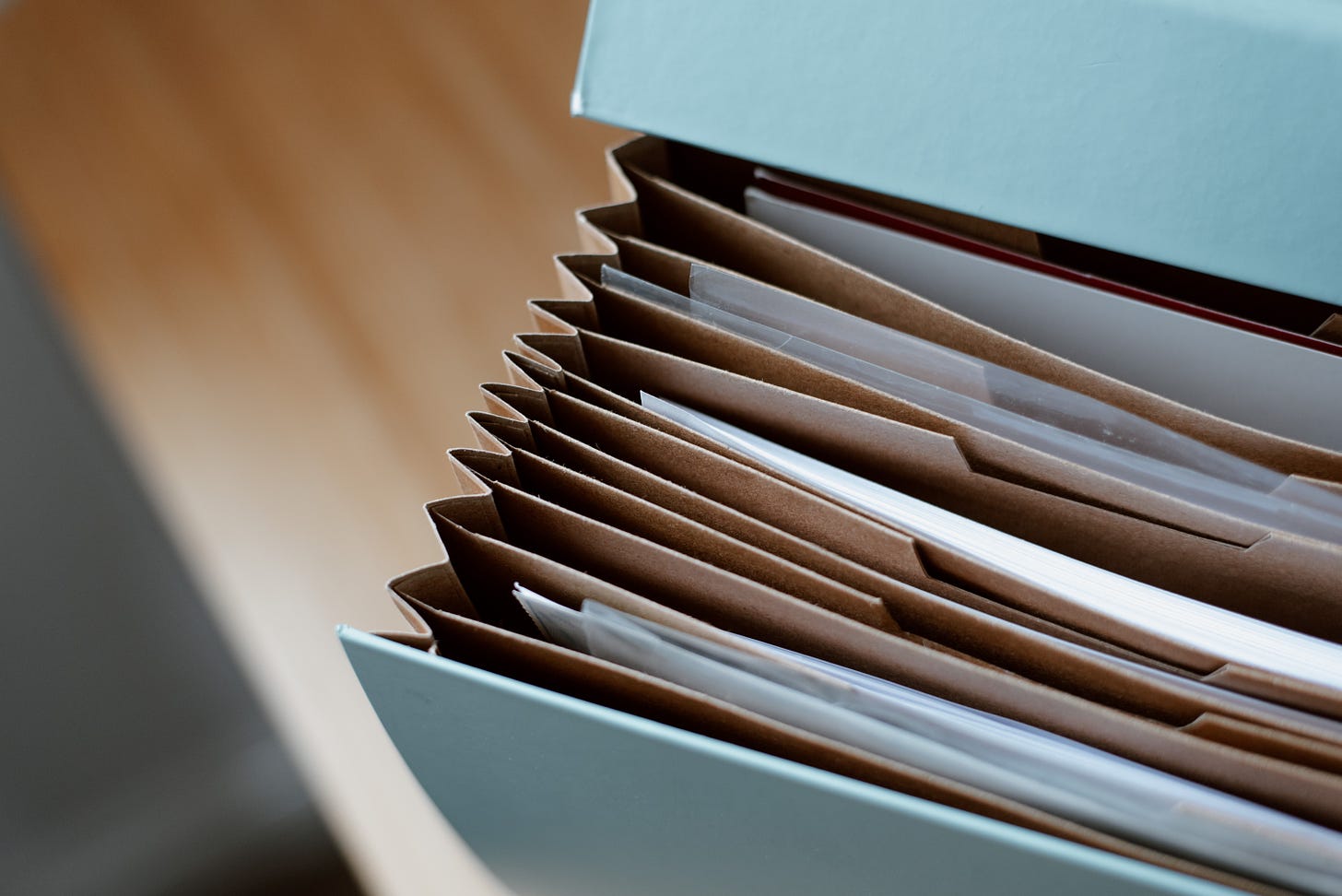 A blue container with brown file folders. White papers are inside some of the folders.