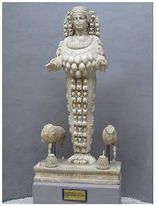 A statue of a woman wearing an elaborate headdress and clothing, her arms partially extended in front of her body.