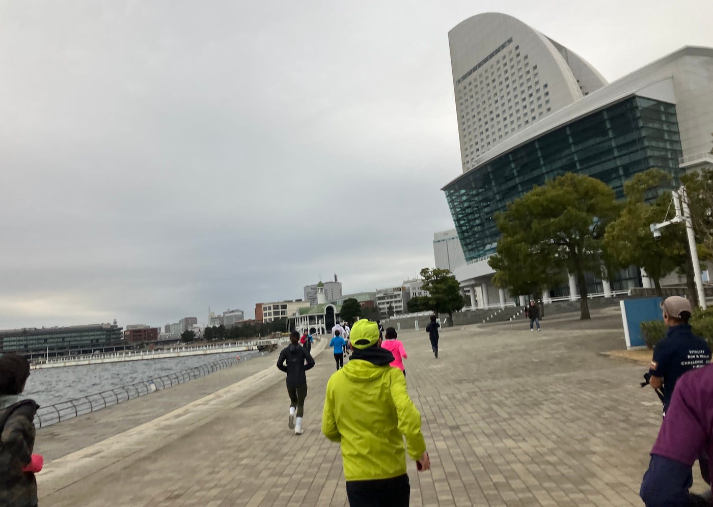 Runners on the bay walk, port to the left, large buildings to the right