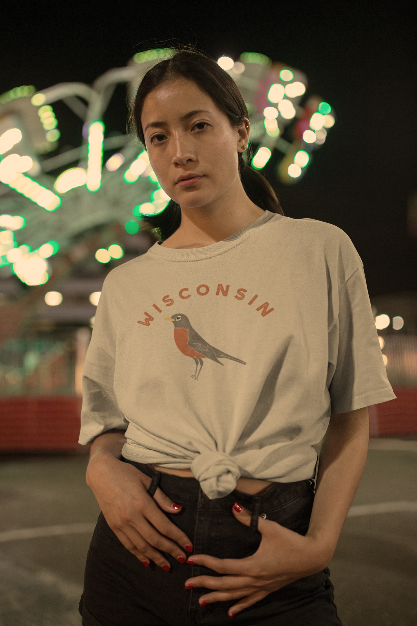 Woman at a carnival at night wearing a t-shirt that reads "Wisconsin" and has an illustration of an American robin.