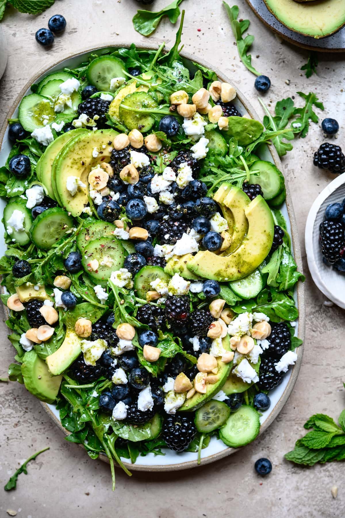 overhead view of blackberry avocado arugula salad on a white platter