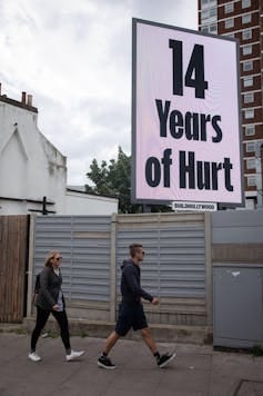 A poster reading '14 years of hurt' with two people walking past.