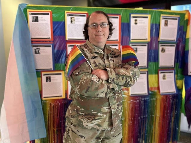 A person in military uniform holding a rainbow flag

Description automatically generated