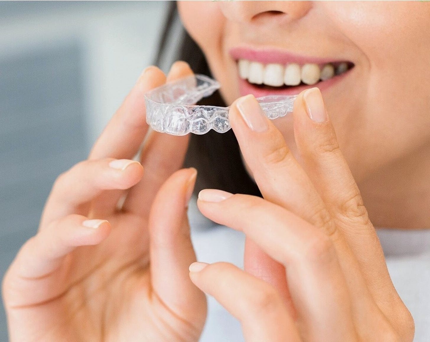 A closeup of an anonymous woman holding an Invisalign aligner close to her mouth.