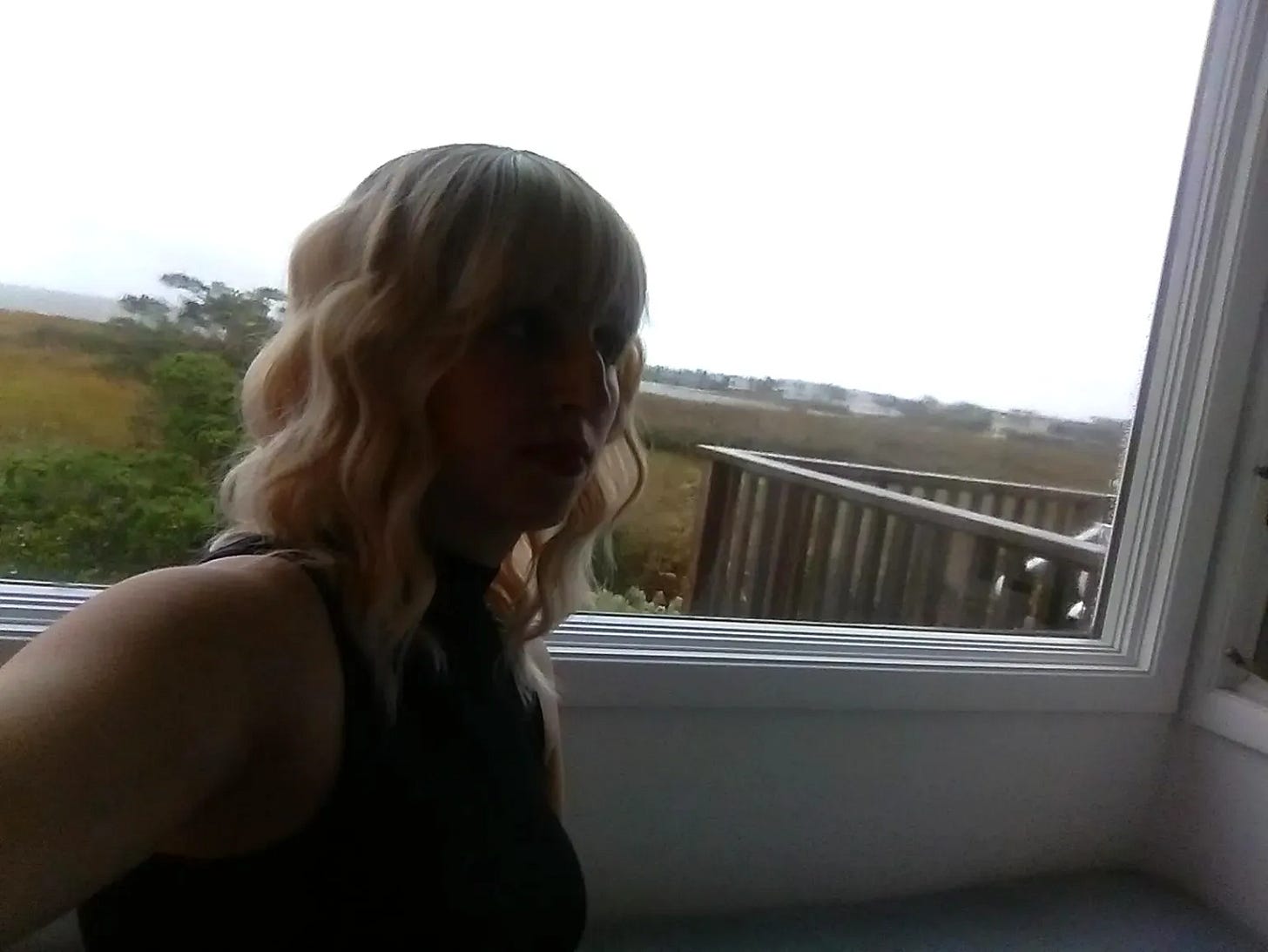 The film’s director, Rebecca Shoptaw, wears a blonde wig and sits in front of a window in this behind-the-scenes moment captured on set.