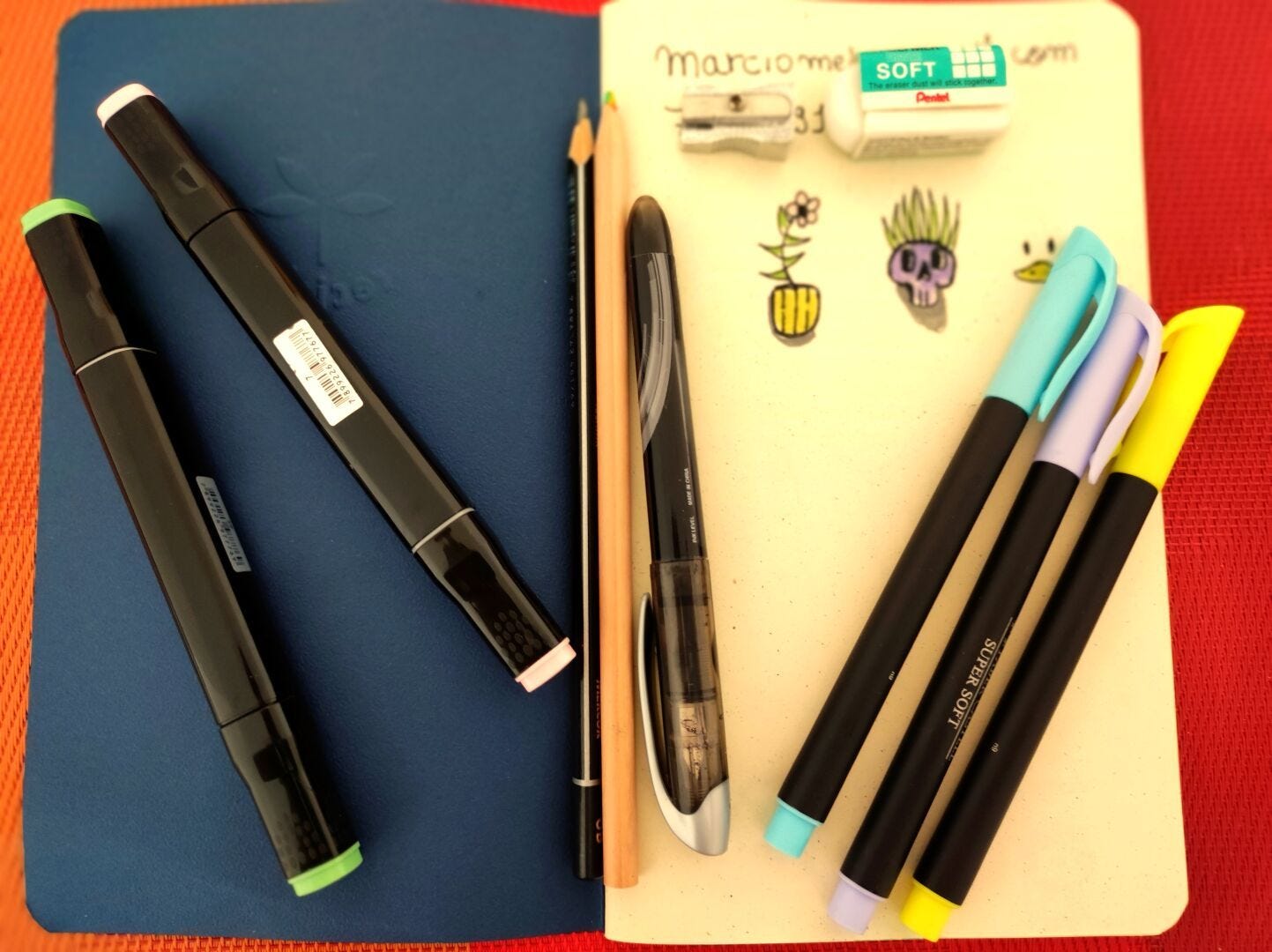 caderneta aberta com canetas, lapis e marcadores espalhados por cima