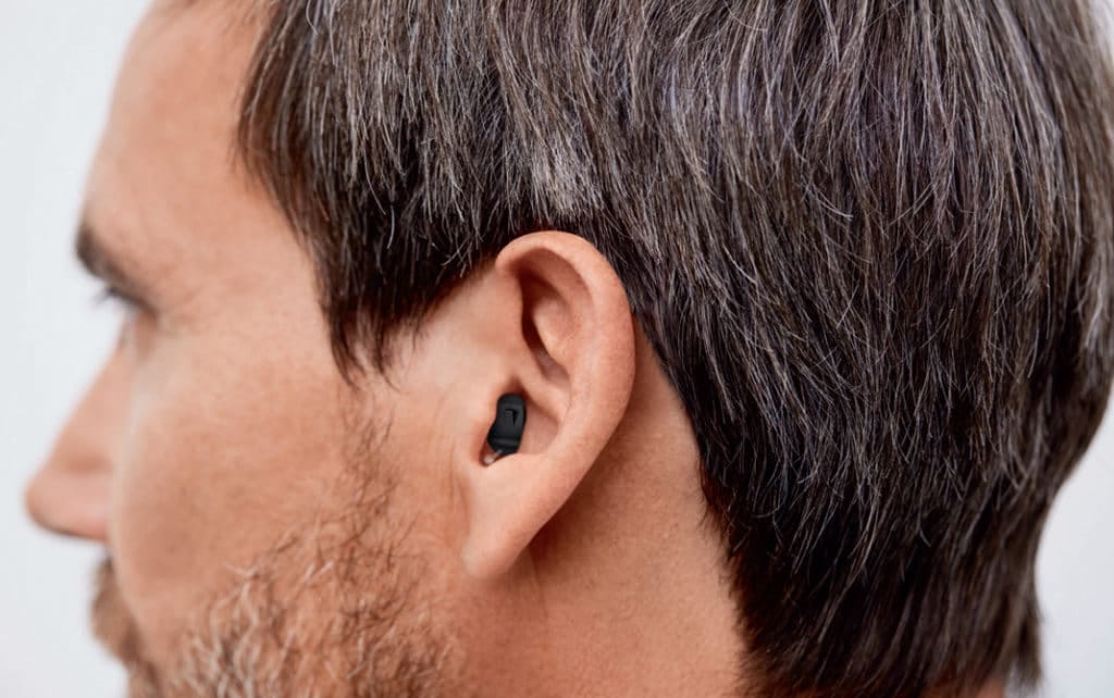 side view of a middle aged man wearing a tiny hearing aid, one that fits neatly into the ear hole, almost imperceptible