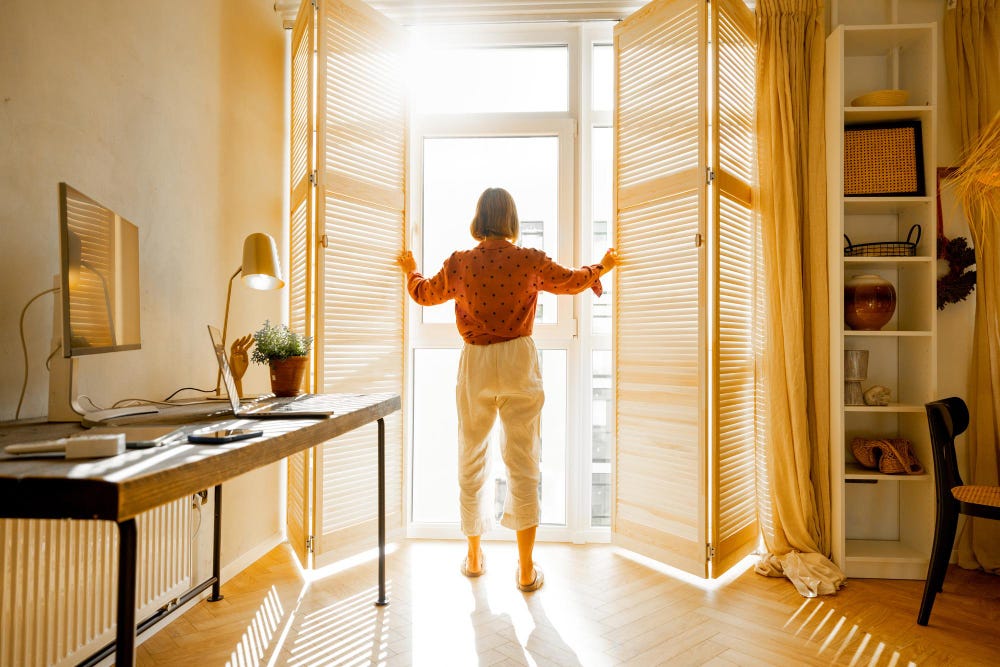Woman open blinds in a sunny room.