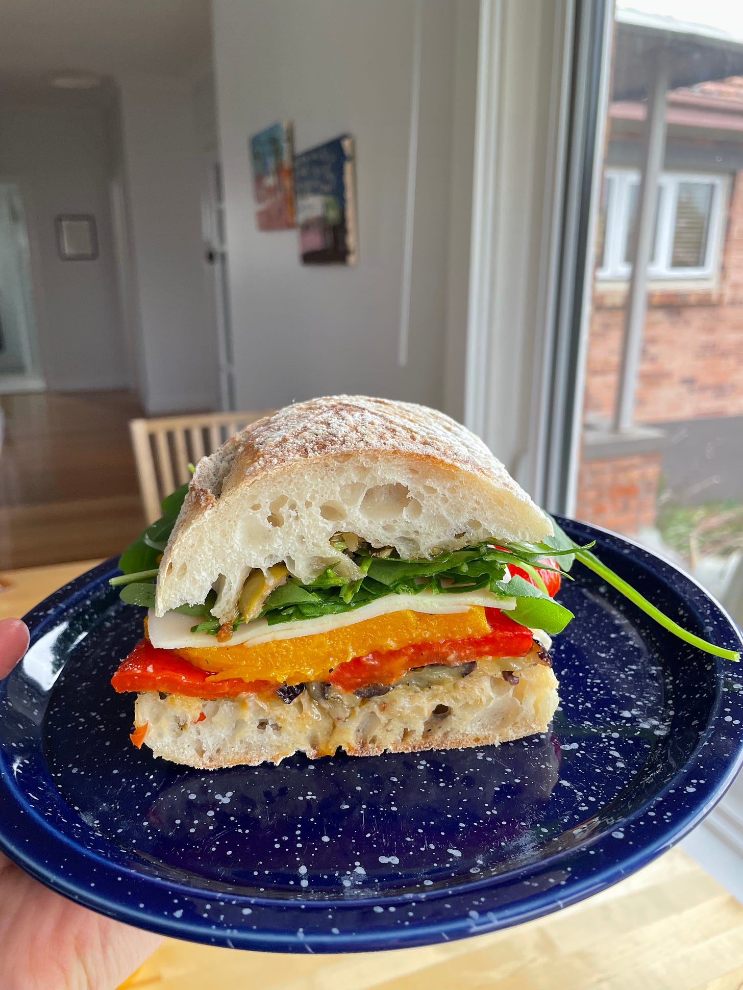 A big slice of a roast veggie sandwich made using a ciabatta with layers of roasted pumpkin, red capsicum, eggplant, provolone cheese and rocket.