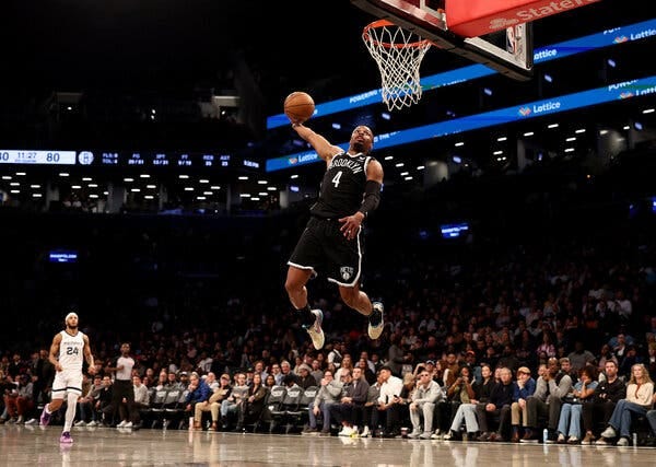 A leaping player for the Brooklyn Nets about to dunk a basketball with no defender near him during an N.B.A. game. 