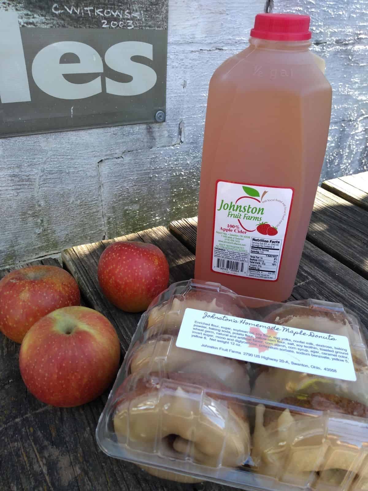 Johnston Fruit Farms apple cider, maple donuts, and apples on a picnic table.