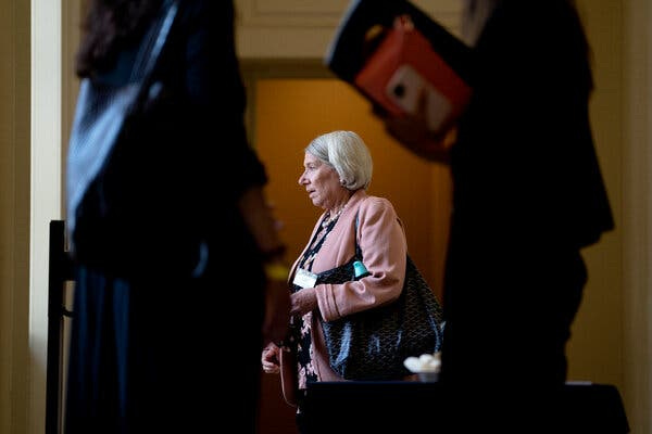 Center of the frame is Anita Dunn. She is wearing a pink blazer with a dark floral prints underneath.