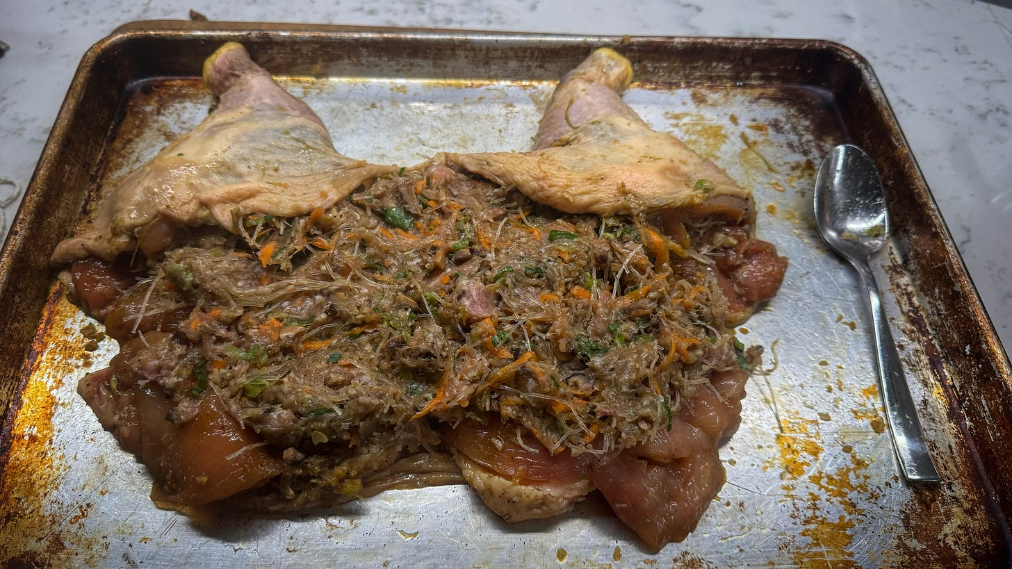 A deboned chicken on a sheet pan, covered in a stuffing of glass noodles, ground pork, vegetables, and seasoning.