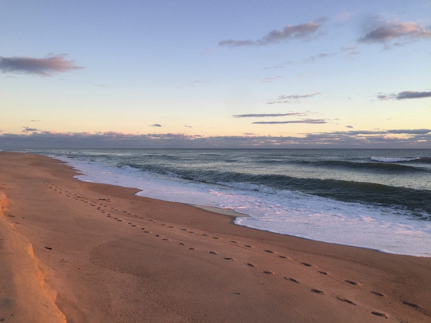 View of a beach at sunset, with white foamy surf and golden sand.