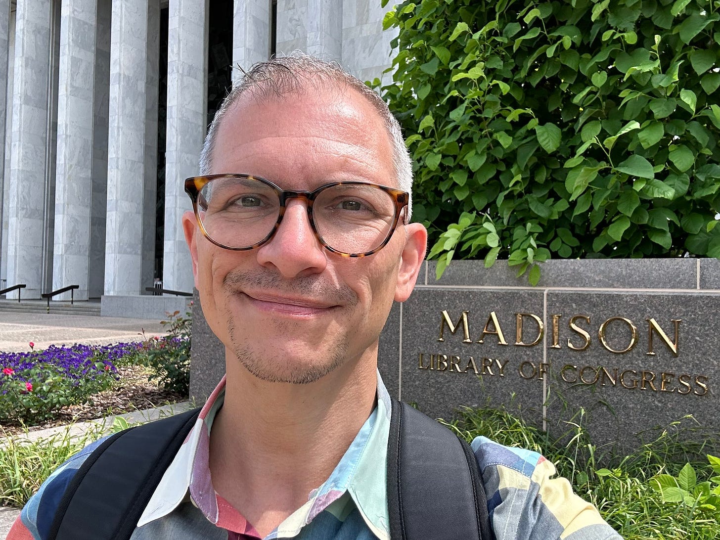 Chris in a spring-colored check shirt in front of the Madison building of the Library of Congress.