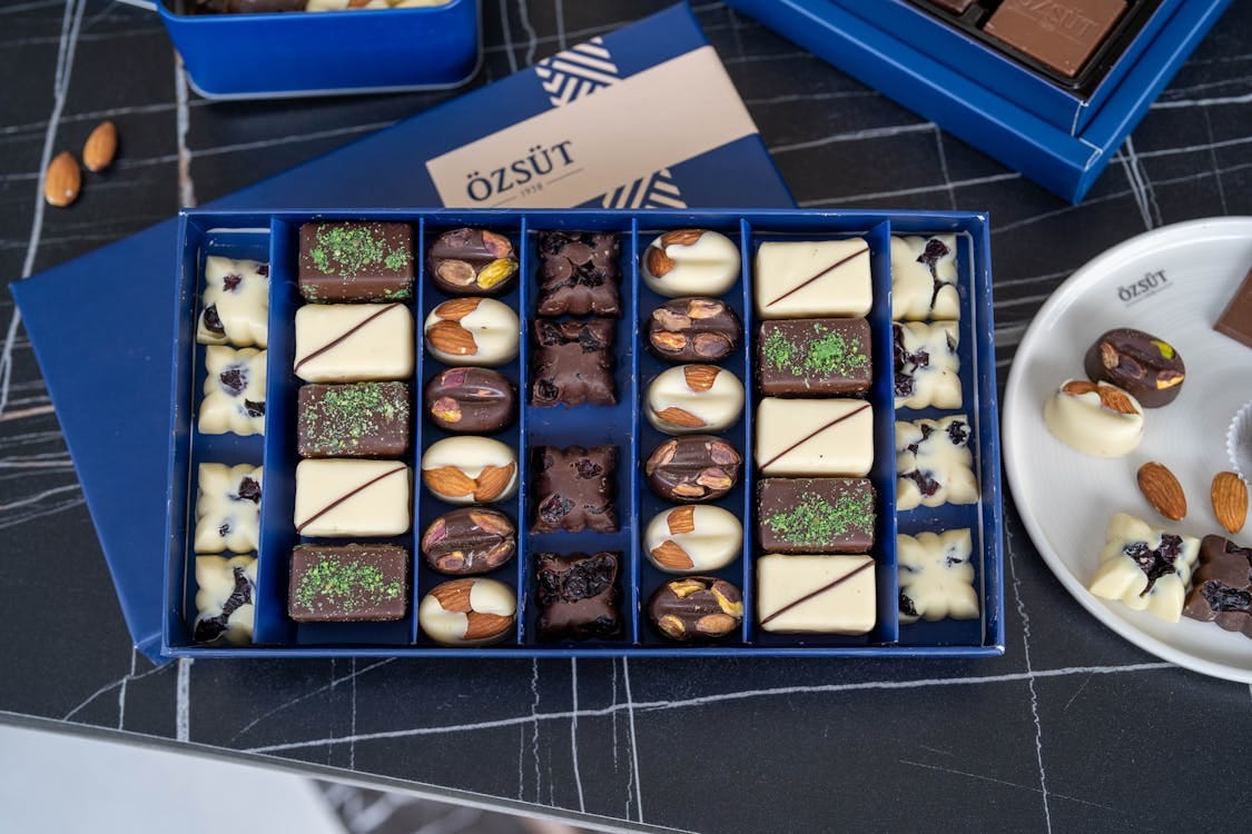 Free Discover a gourmet assortment of chocolates featuring almonds and pistachios in a stylish blue box from Kahramanmaraş. Stock Photo