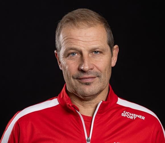 Mann in rotem Trainingsanzug mit Ochsner Sport Logo vor schwarzem Hintergrund.
