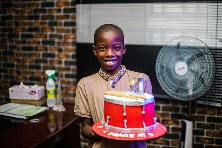 A young boy holding a birthday cake, in his hands, with a happy smile on his face.