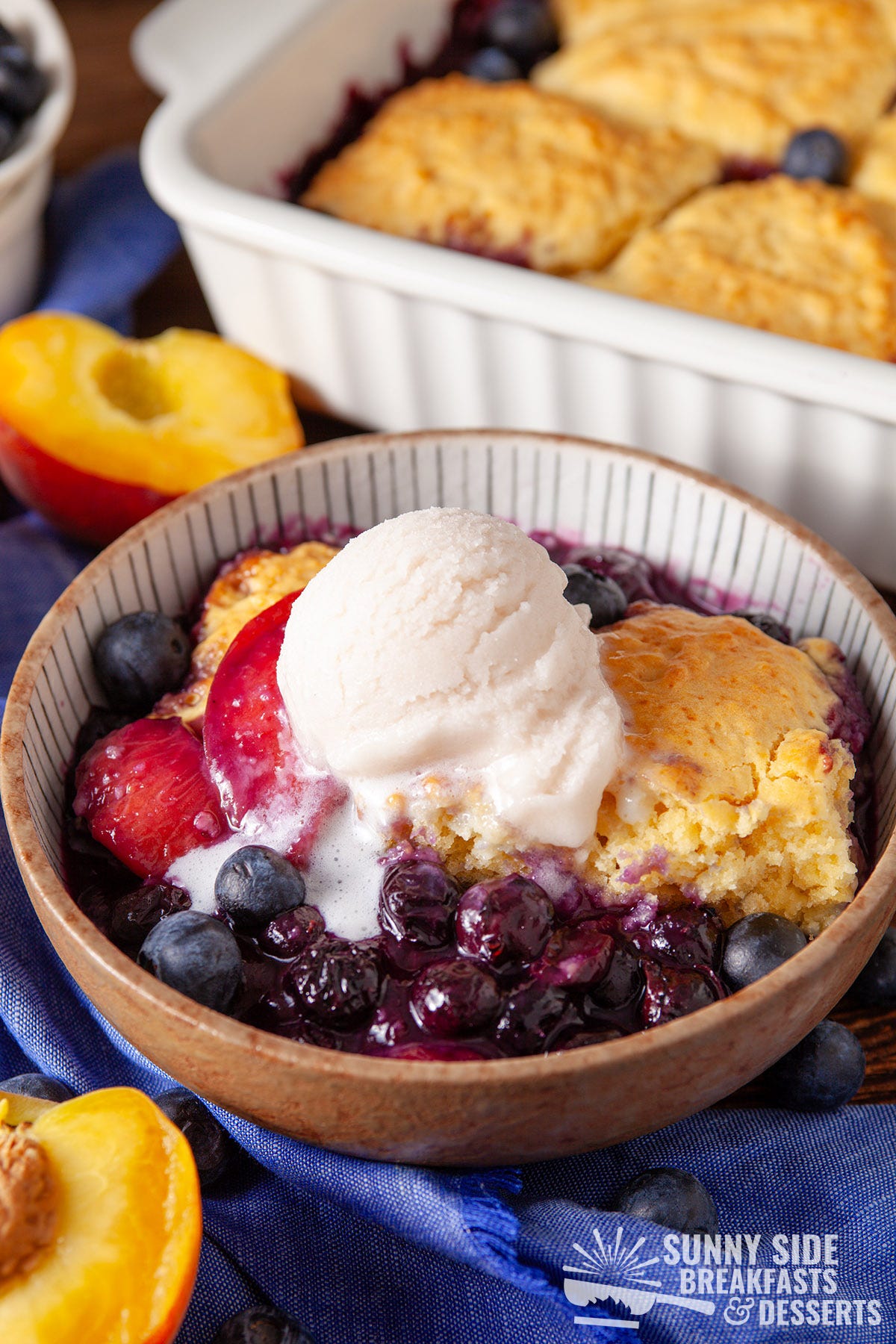 Blueberry peach cobbler in a bowl with ice cream.