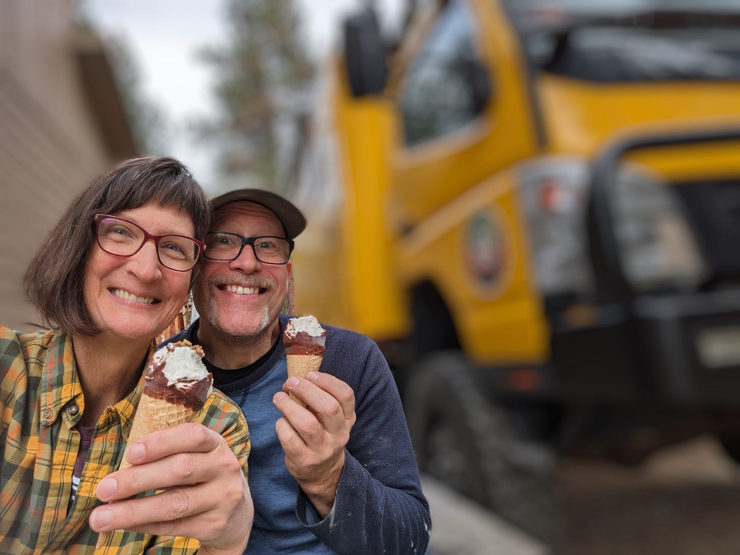 my husband and I with ice cream cones, smiling, in front of a blurred out yellow truck