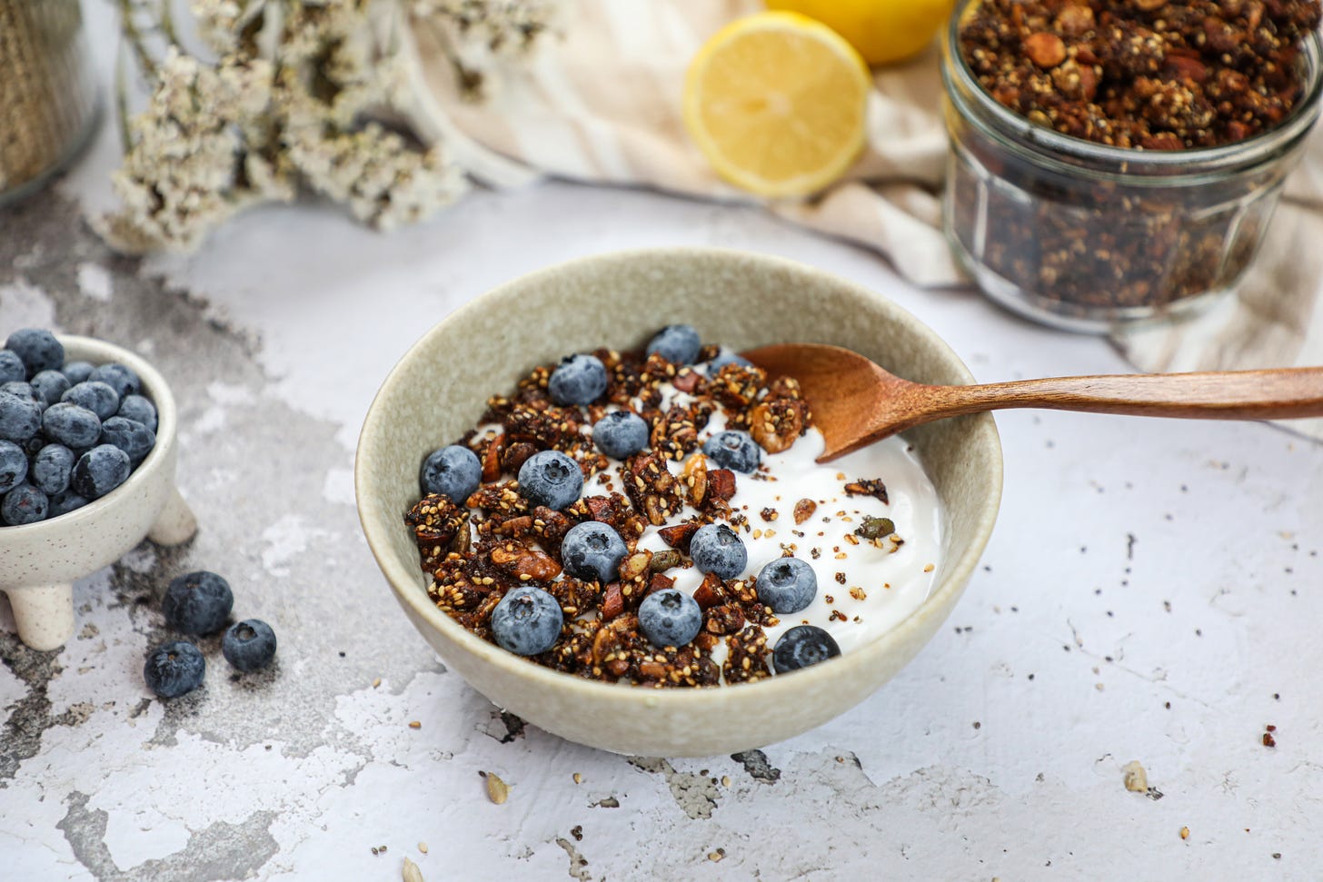 Small bowl of blueberries, bowl of yogurt with granola and blueberries on top, jar of granola