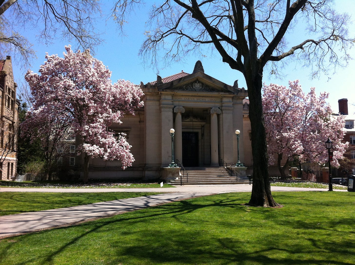 Neoclassical building framed by cherry trees in the background; lawn and leafless trees in the foreground.