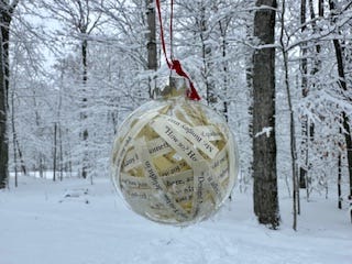 A hanging clear ornament with snowy trees behind it