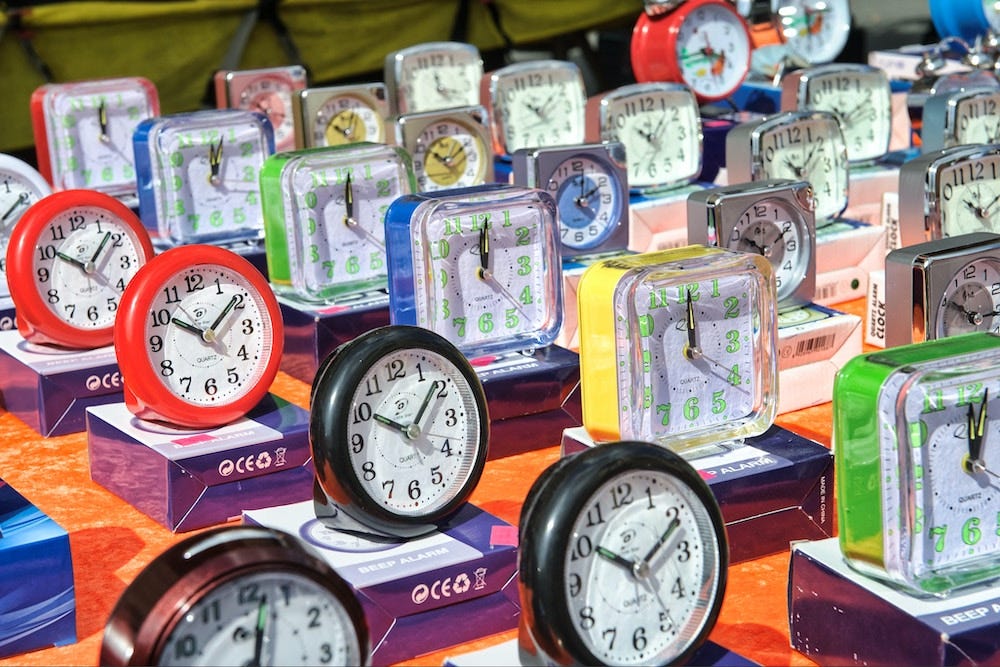 A photograph of a market stall which has many cheap alarm clocks of all different colours