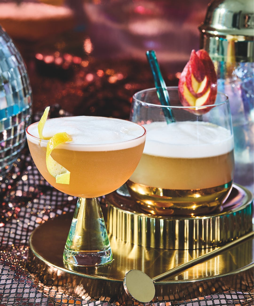 Two amaretto sours--one up and one in a rocks glass--on a gold tray next to a disco ball