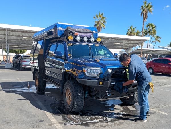 a man washes a blue pickup truck in a grocery store parking lot