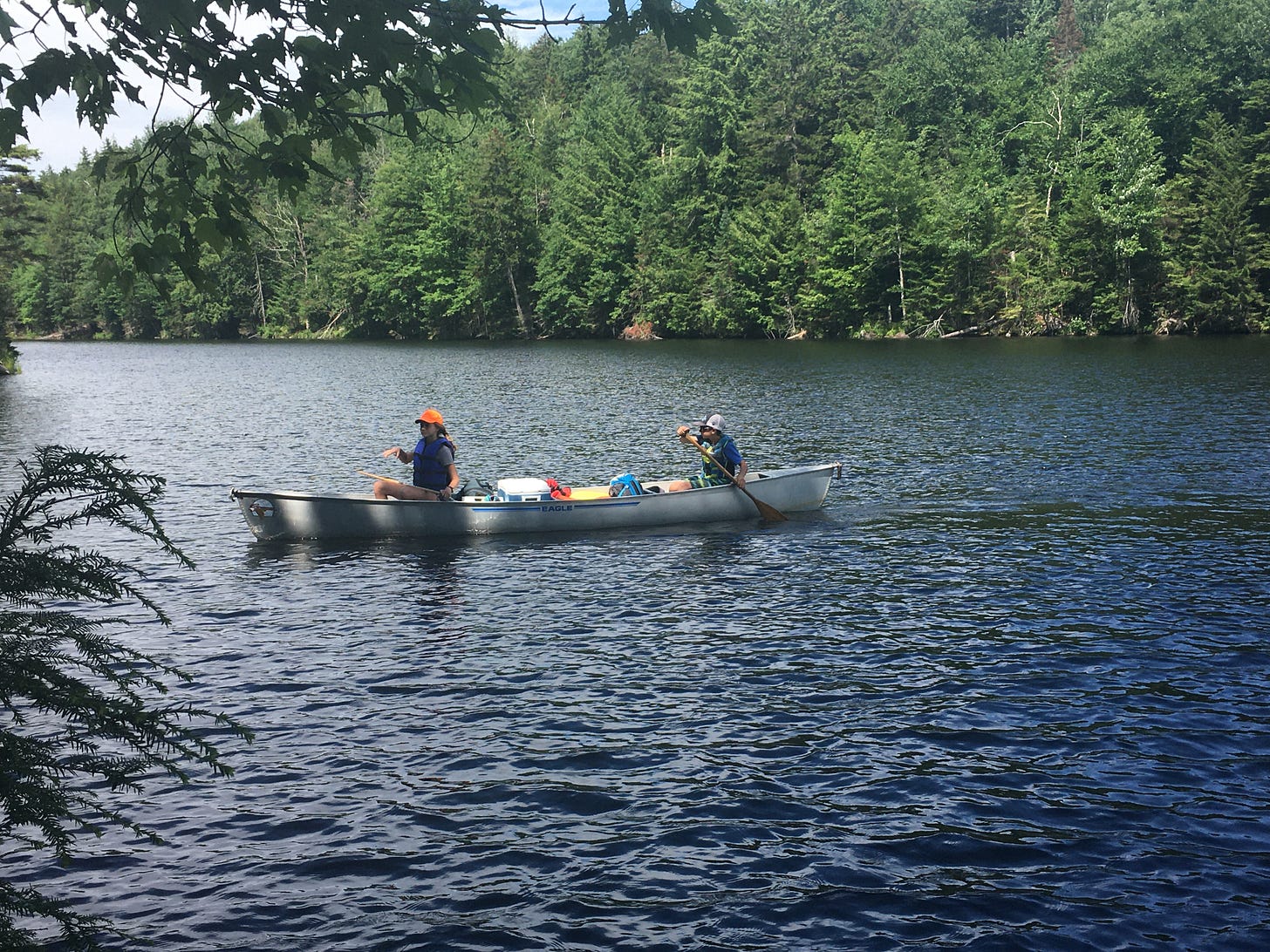 Two kids paddling a loaded canoe on a Vermont pond.