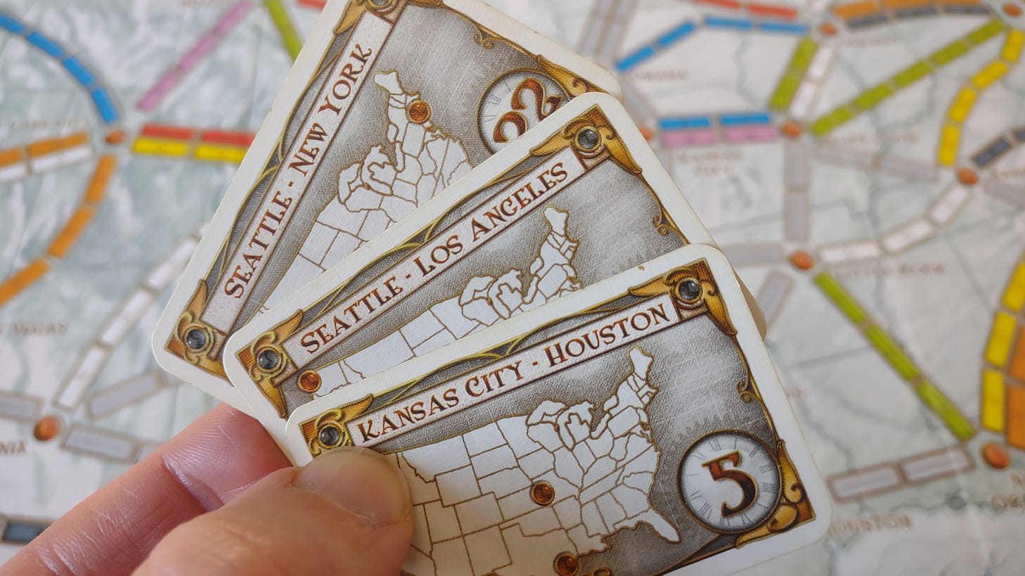 Three cards with cities marked on them are held in front of a map with train routes drawn on it.