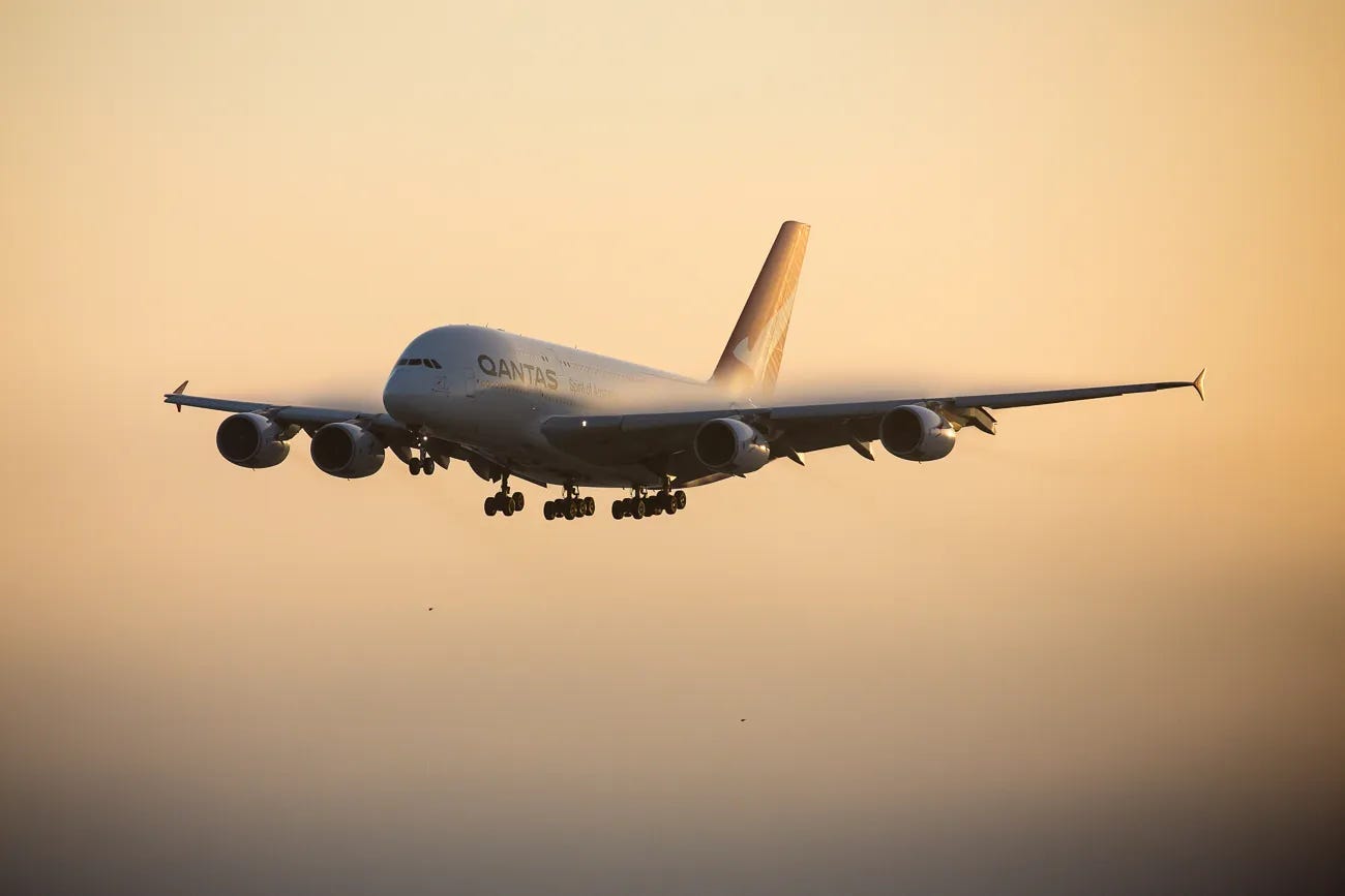 A Qantas Airbus A380 aircraft in flight against a golden sky during sunset or sunrise.