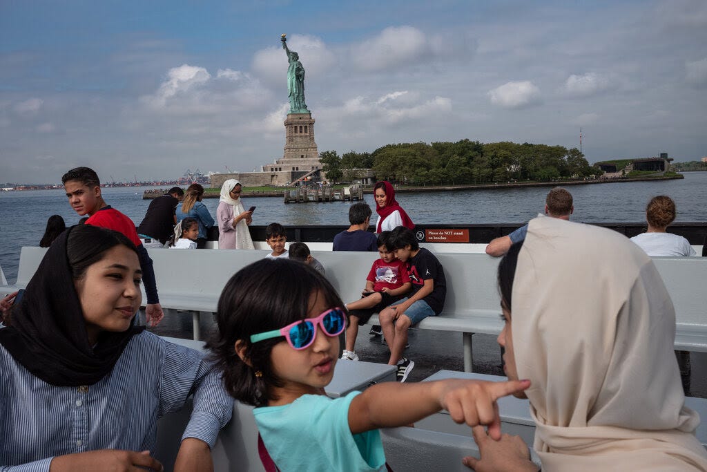 Passengers on a ferry passing by the Statue of Liberty. In the foreground are a child and two women wearing head scarves.