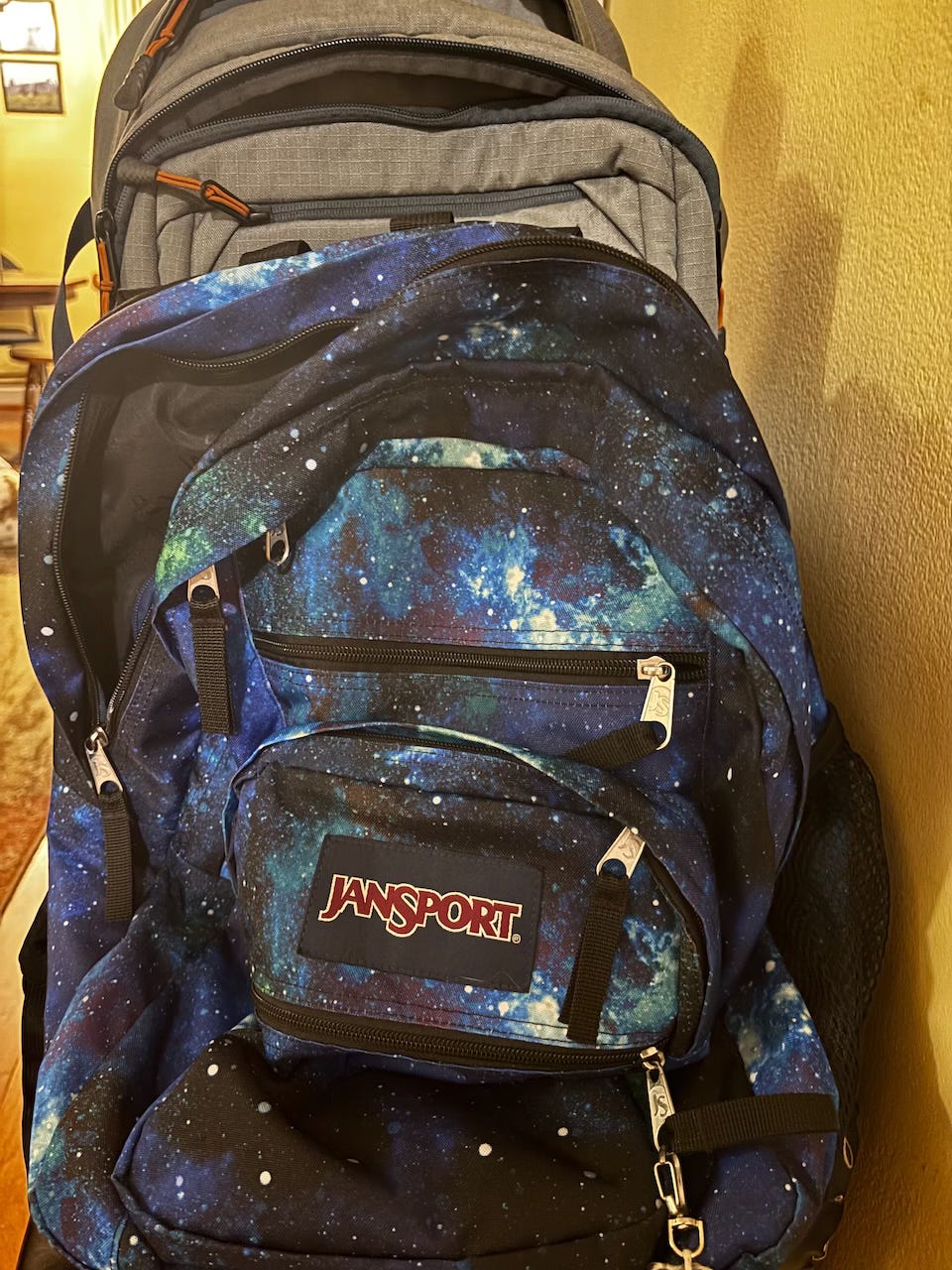 Two backpacks, one with a space design on it and another a plain gray